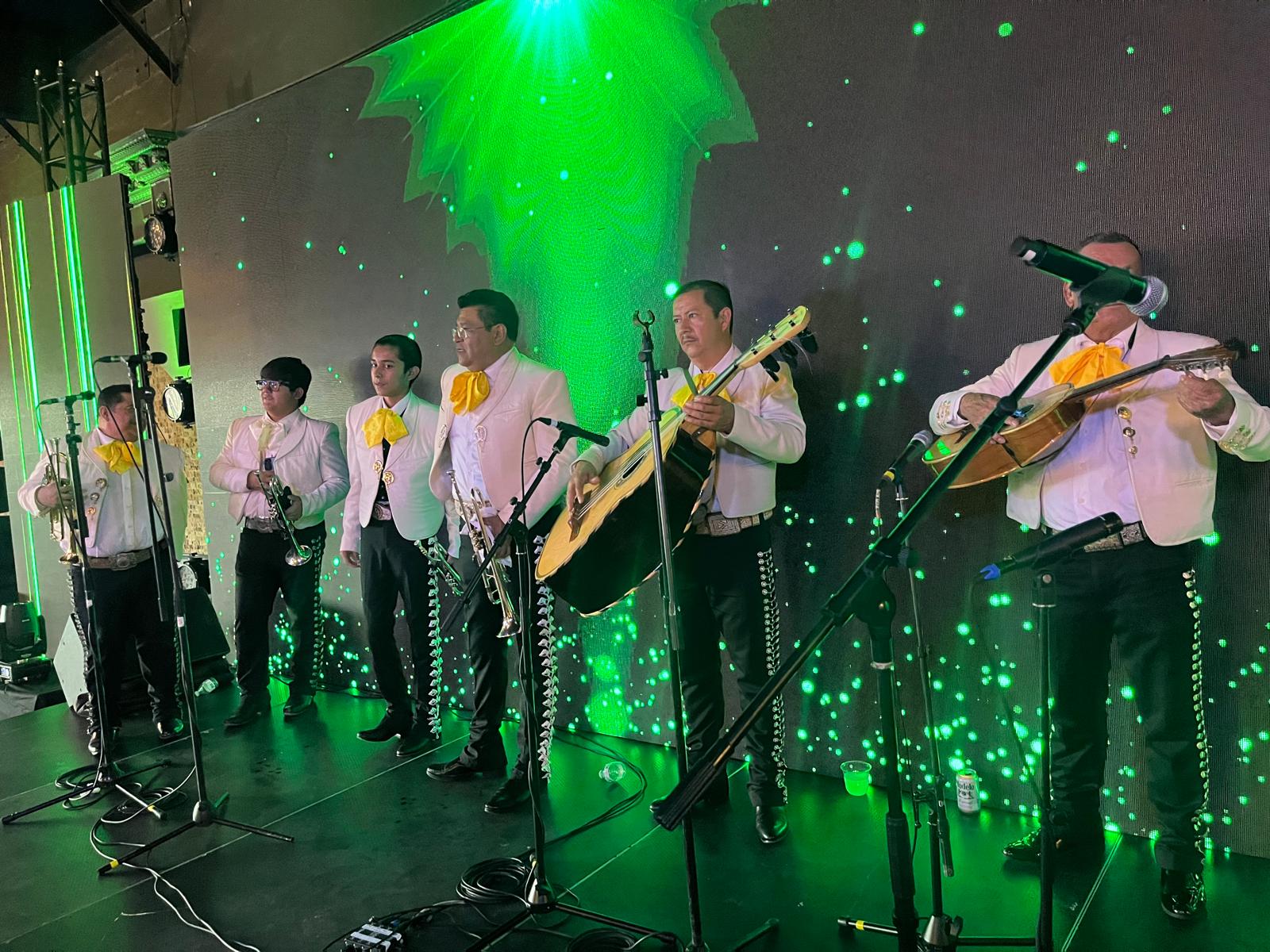 Mariachi musicians performing on a stage lit in green